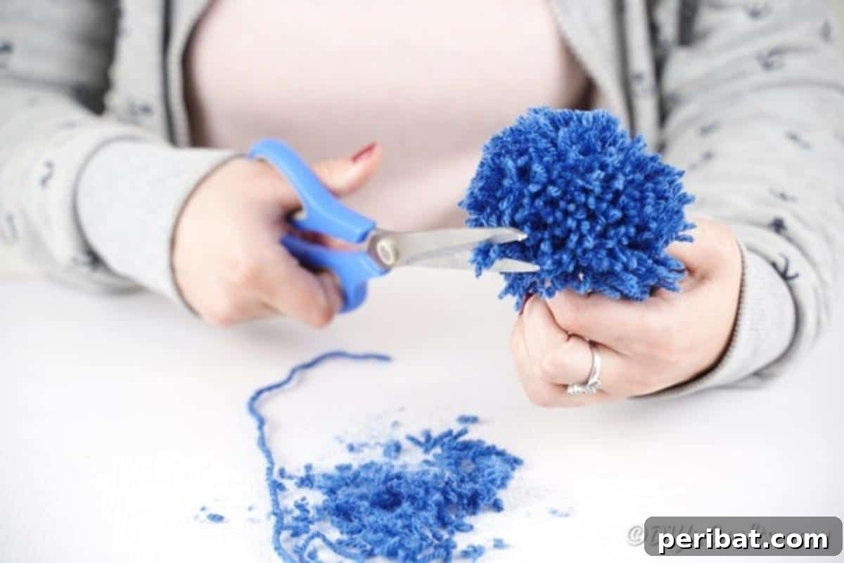Scissors cutting the yarn loops and shaping the pom pom