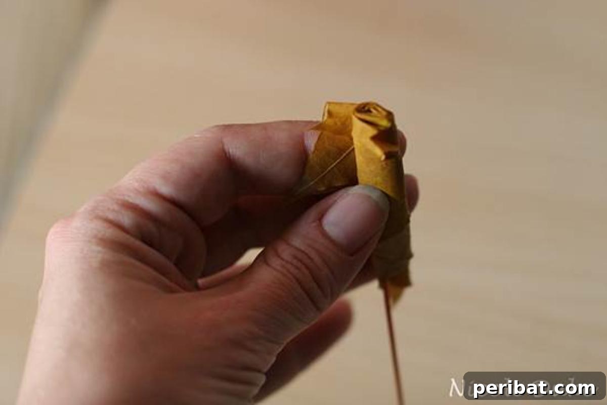 A maple leaf being tightly rolled from right to left, forming the central core of a DIY leaf rose.