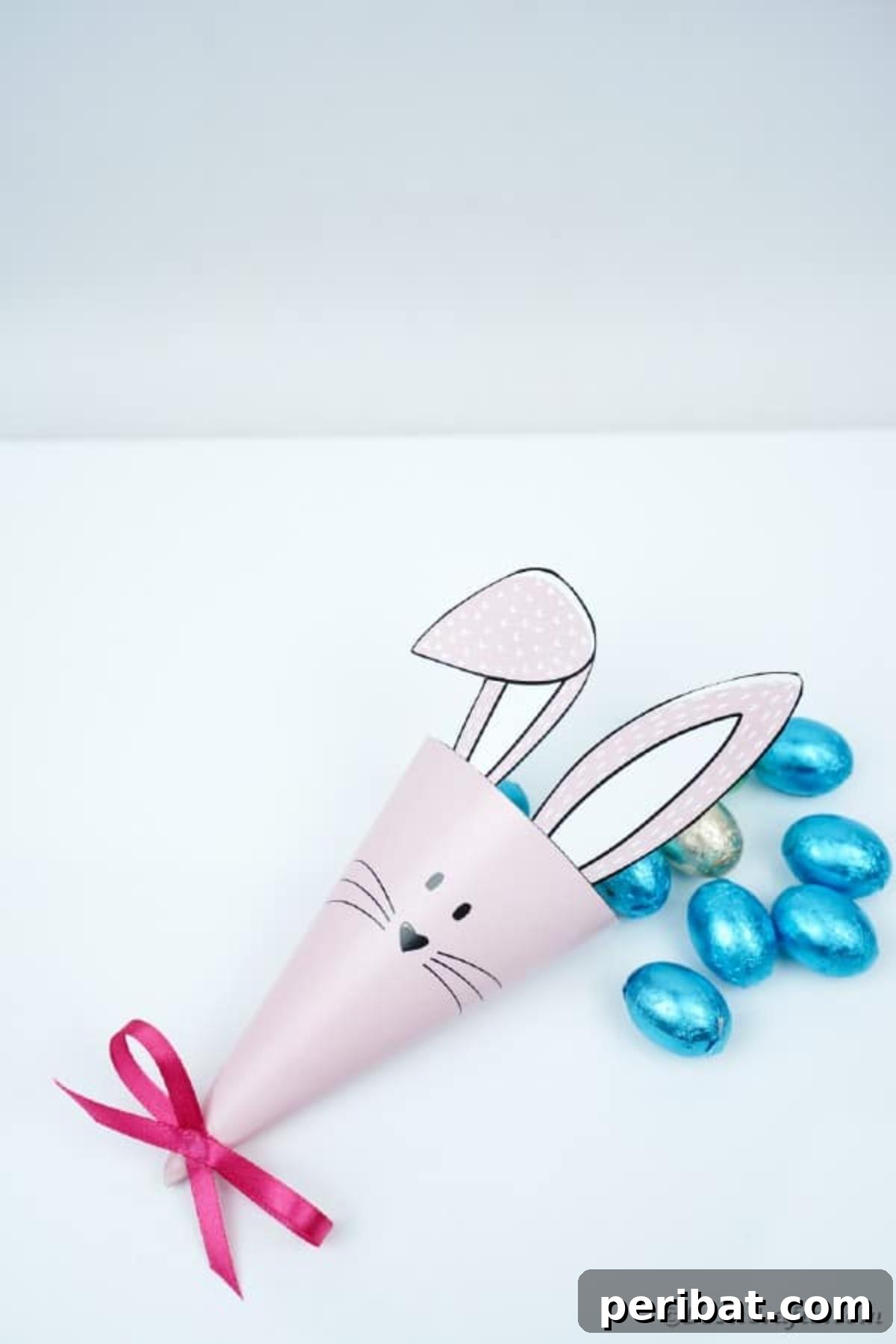 Free Easter Bunny Treat Holder Template 14 Finished paper bunny cone on a white table, filled with blue candies