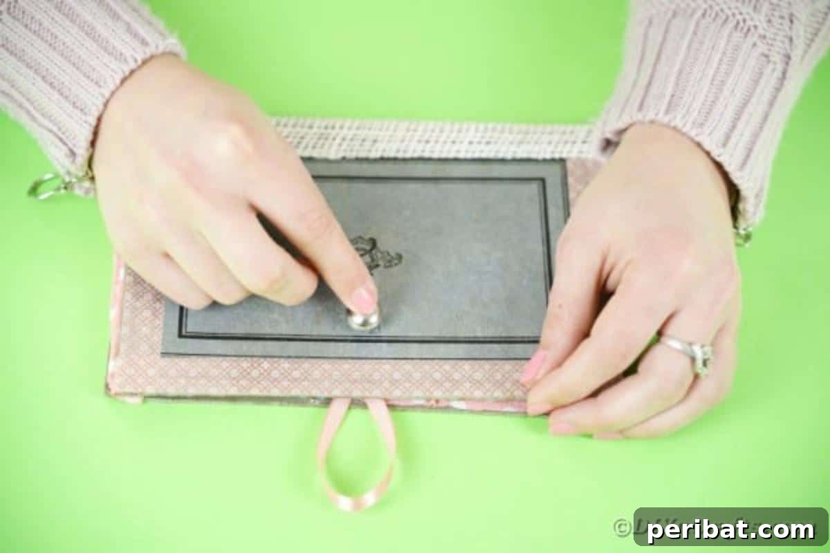 Old Books New Fashion DIY Book Purse Tutorial 15 Carefully gluing a small silver button onto the front exterior of the book purse, ensuring precise alignment with the ribbon loop for a secure closure
