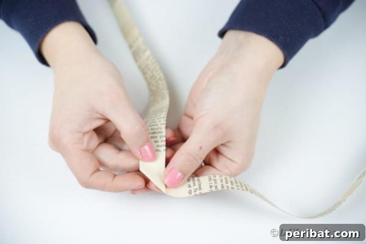 Hands engaged in the intricate folding of book page strips into a continuous 3D accordion pattern, forming a paper chain.