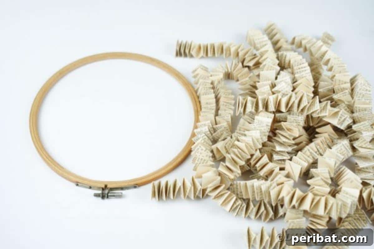 Several neatly folded paper chains (book page ribbons) laid out next to an embroidery hoop, ready for assembly.