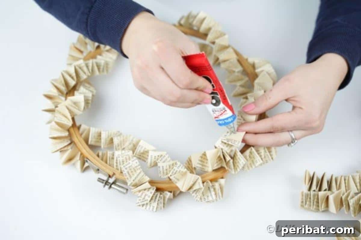 Hands gluing a folded paper chain onto an embroidery hoop, beginning the assembly of the wreath.