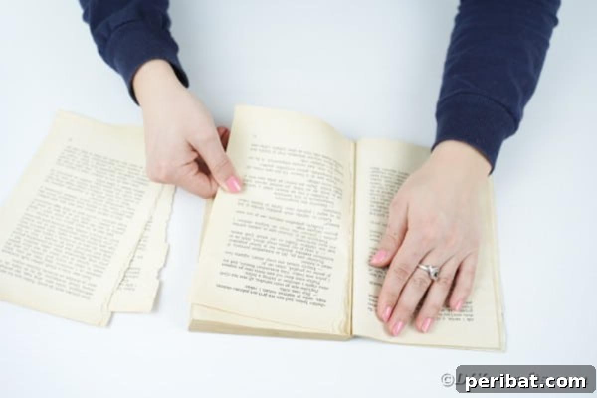 Hands carefully tearing pages from an old book, preparing them for the wreath craft.