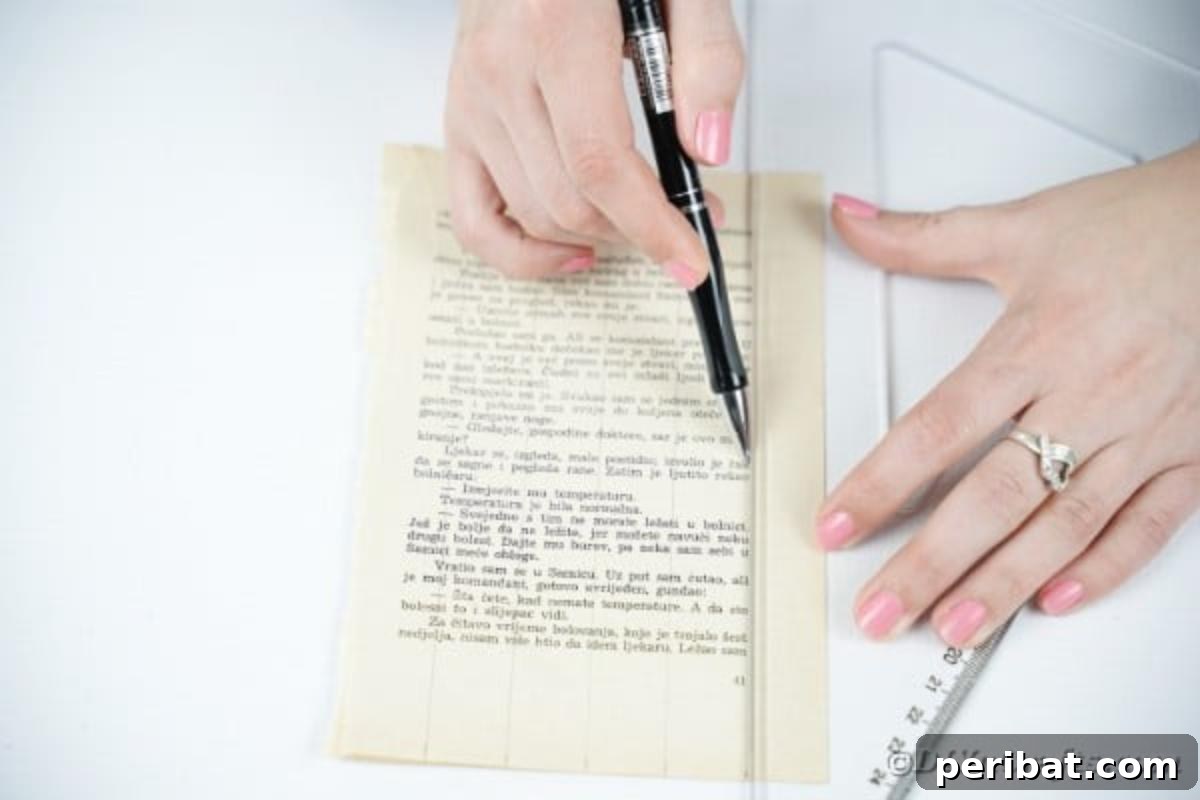 A ruler and pen being used to measure and mark lines on book pages, preparing them for cutting into strips.