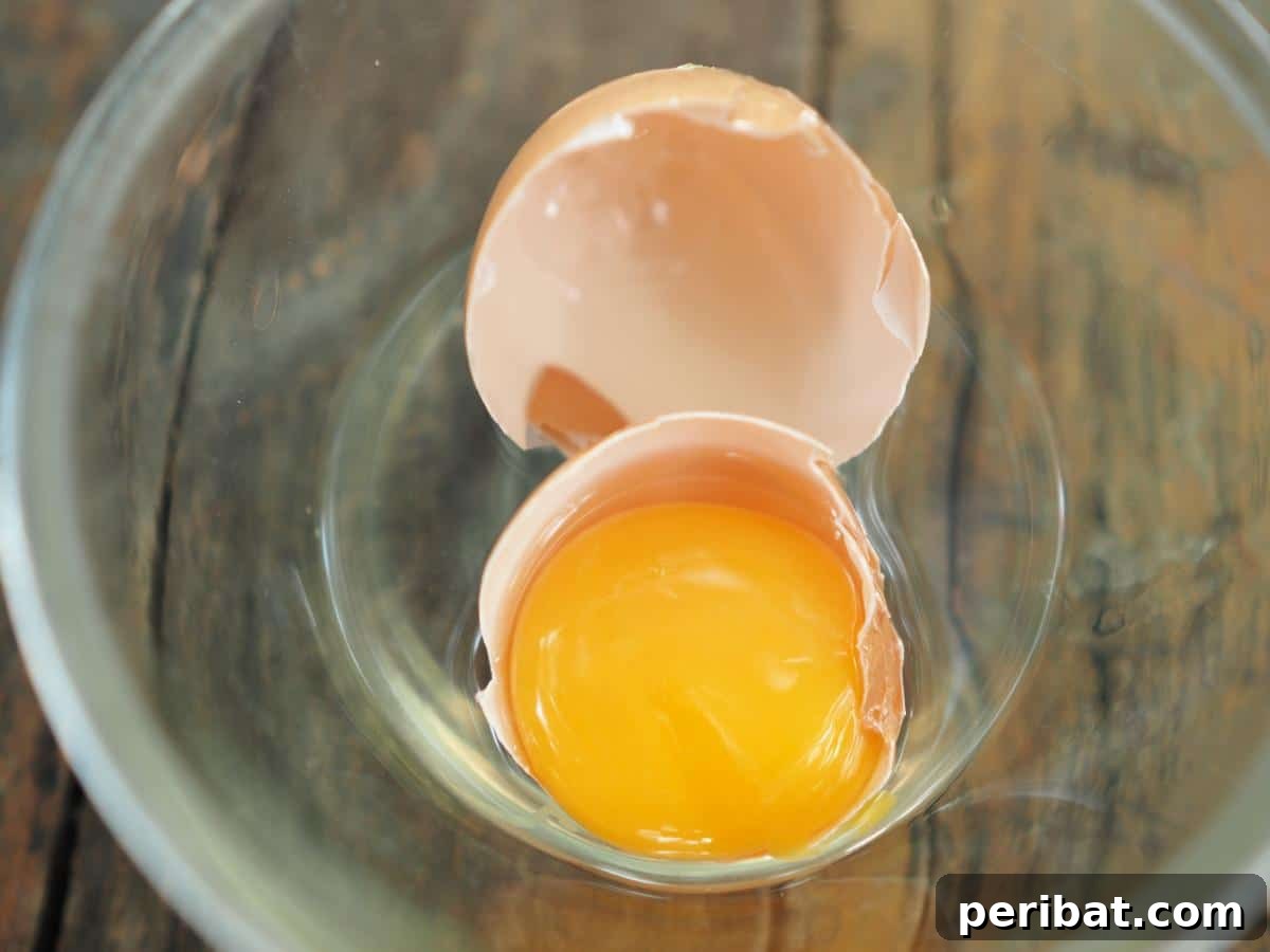 A cracked egg in a glass bowl, illustrating the essential step of removing shells before freezing eggs.