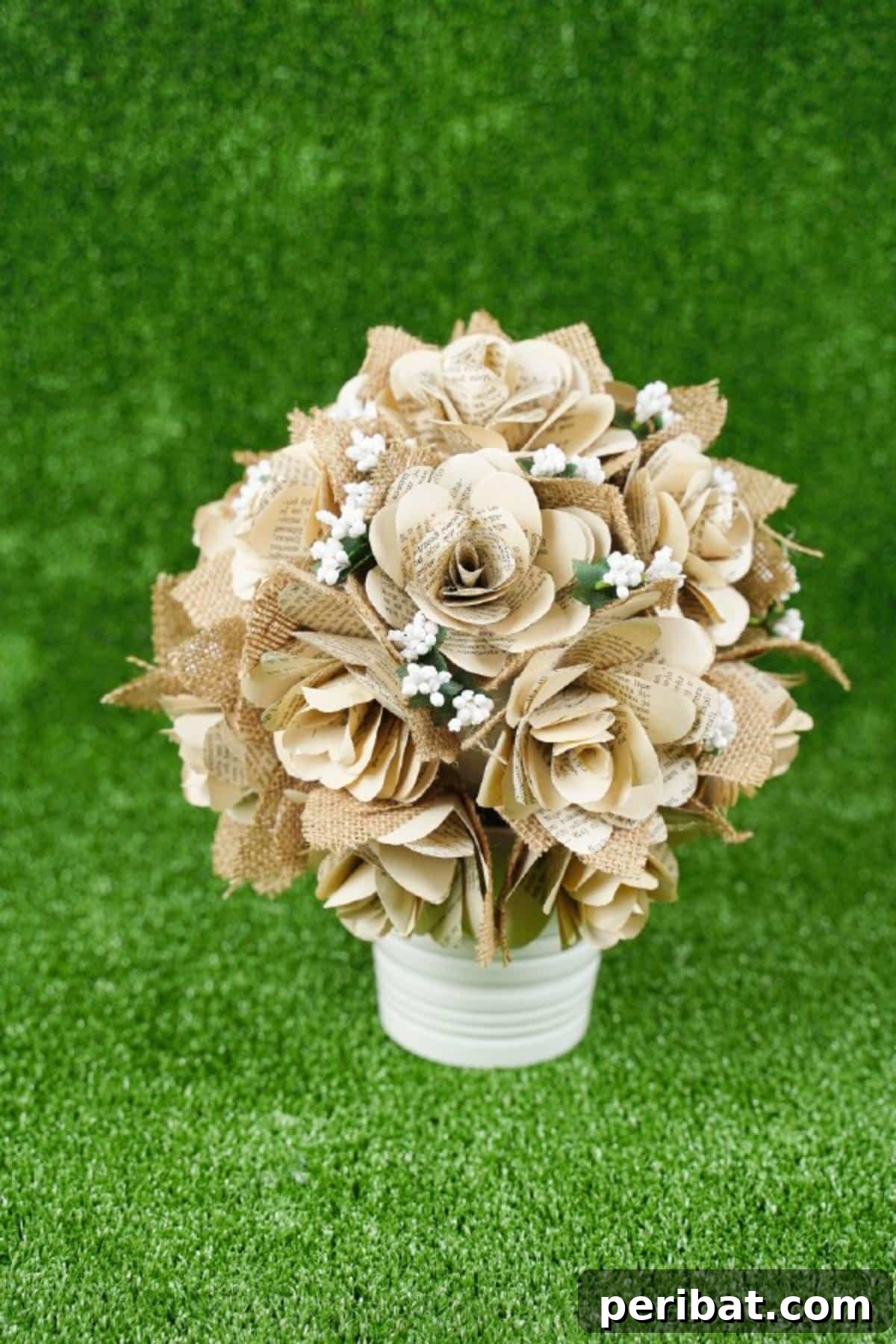 Close-up of an old book page rose ball nestled on green grass, highlighting its rustic beauty