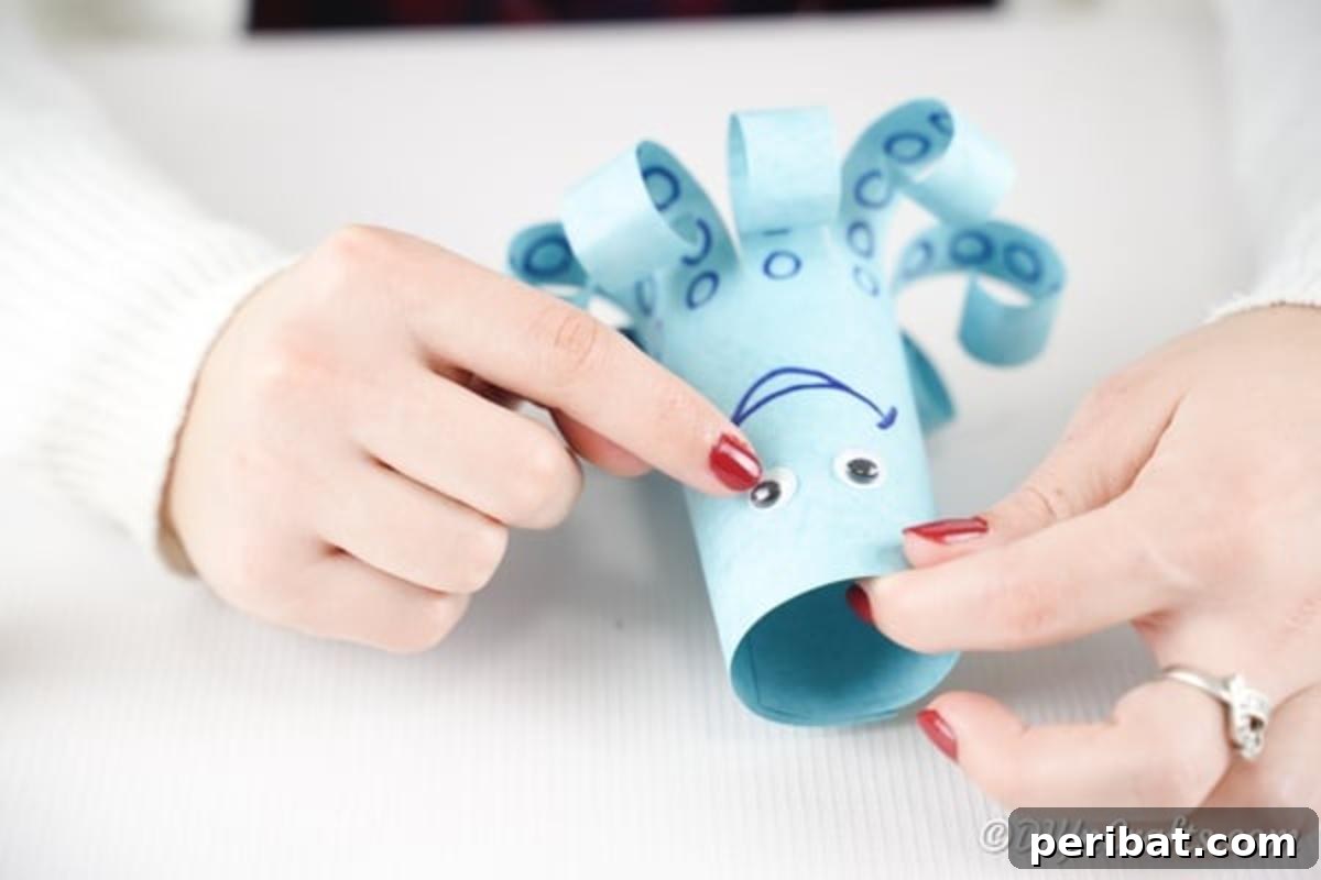 Attaching googly eyes to the paper octopus's face, above the drawn smile.