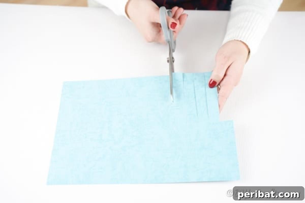Hand cutting strips halfway up a blue piece of paper for the octopus craft.
