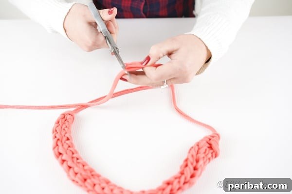 The final step of tying off the end of a finger knit necklace, ensuring it is secure.
