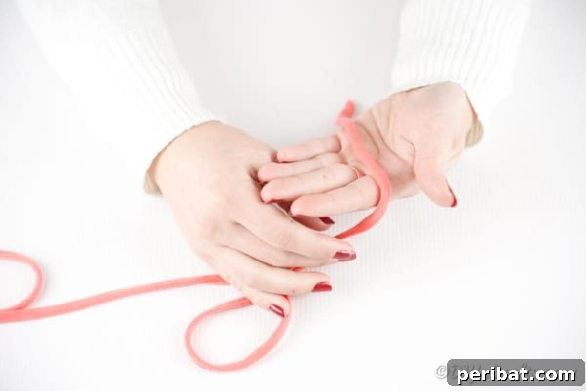 Effortless Elegance: Finger Knit Necklace DIY Video Tutorial 7 Initial step of weaving pink yarn over the palm and between fingers to start the finger knitting process.