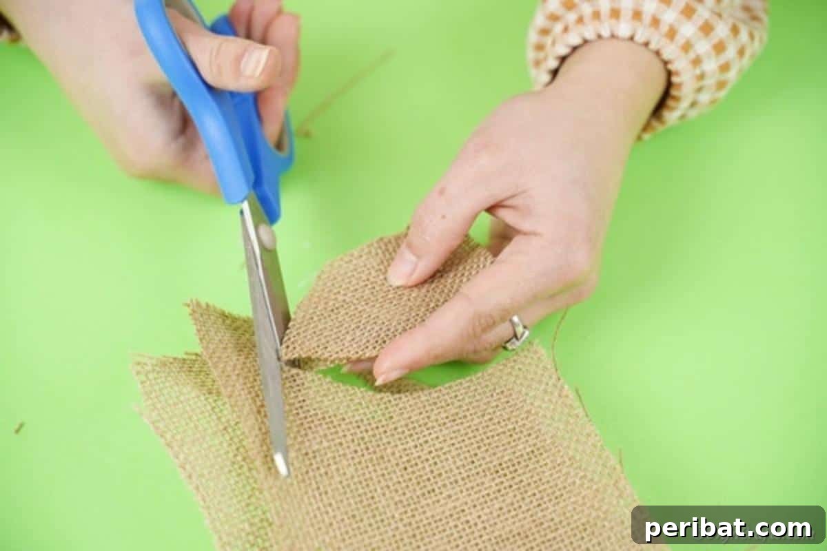 Hoppy Wine Glass Bunny Decor Tutorial 12 A hand using scissors to cut two ear shapes from a piece of burlap fabric.