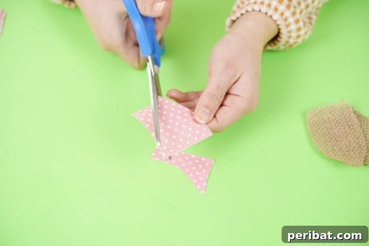 Hoppy Wine Glass Bunny Decor Tutorial 13 A hand using scissors to cut two smaller ear shapes from a piece of pink fabric.