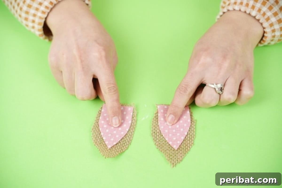 Hoppy Wine Glass Bunny Decor Tutorial 14 A hand using a hot glue gun to attach a pink fabric ear onto a burlap ear.