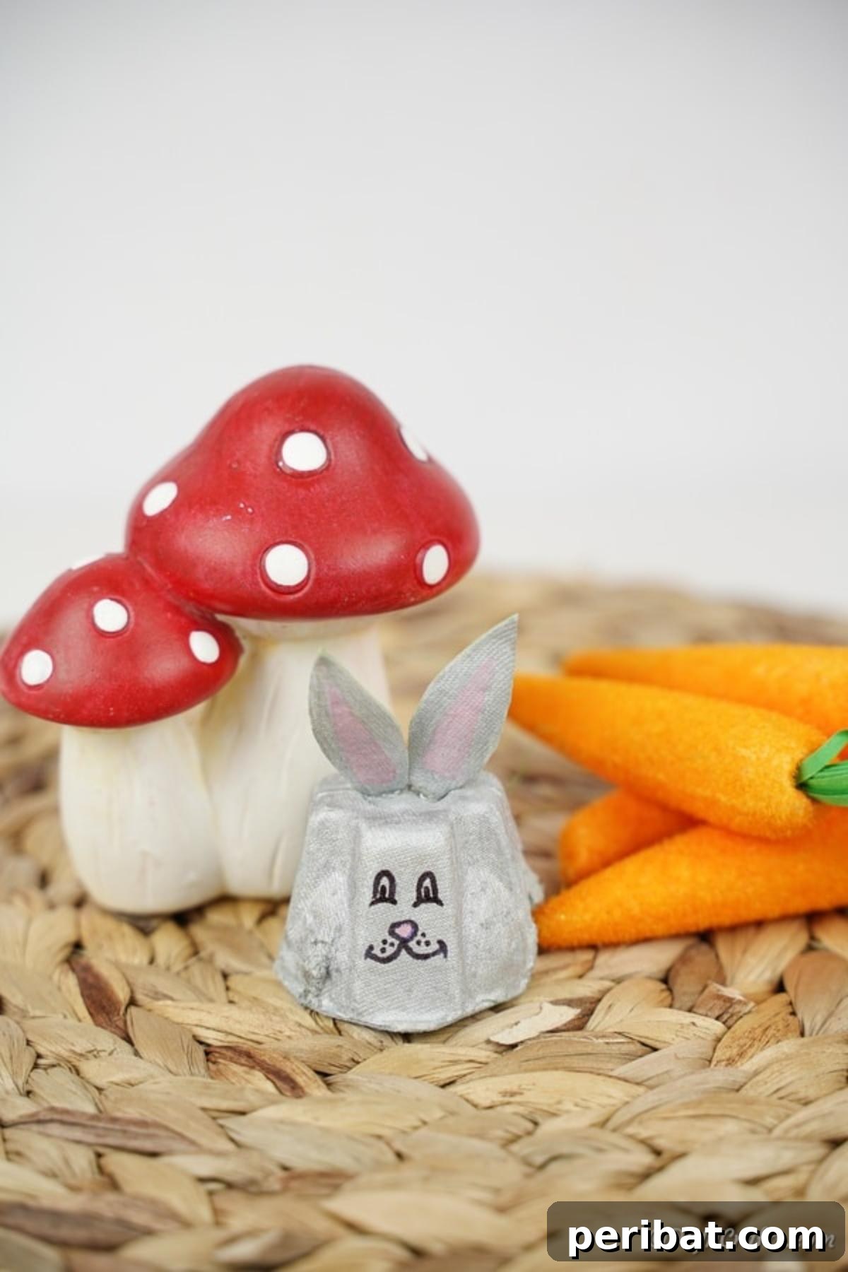 Adorable Upcycled Egg Carton Easter Bunny Craft 5 A delightful egg carton bunny, beautifully painted and detailed, sits on a textured woven mat, accompanied by whimsical mushroom decor, creating a cozy and enchanting display.