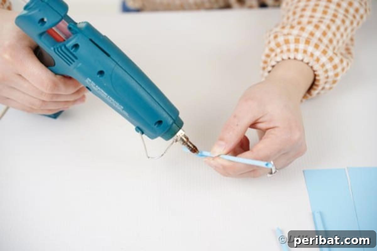 Vibrant DIY Paper Straw Desk Caddy 12 A close-up of hands applying glue to the end of a rolled paper strip to secure it into a straw shape.