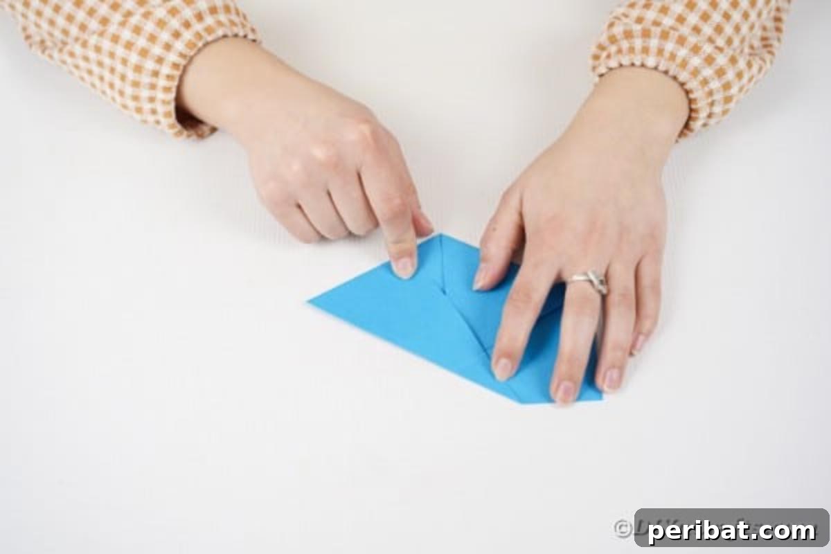Vibrant DIY Paper Straw Desk Caddy 17 Hands are shown carefully folding the bottom edge of a blue paper upwards.