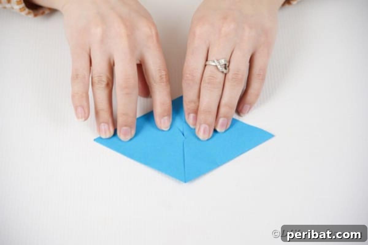 Vibrant DIY Paper Straw Desk Caddy 18 Hands continue folding the blue paper, creating a distinct diamond shape with symmetrical folds.