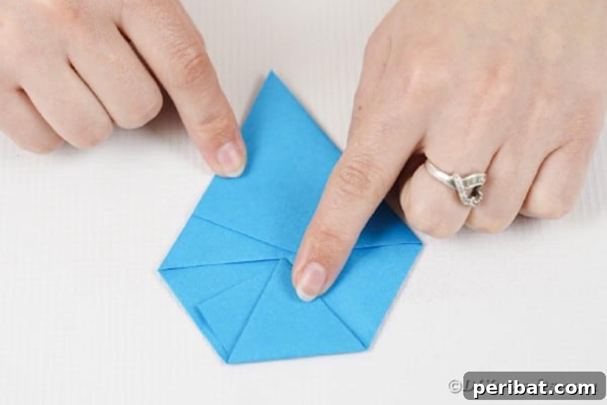 Vibrant DIY Paper Straw Desk Caddy 19 Hands are meticulously folding the final corners of the blue paper inwards to achieve a six-sided polygon shape.