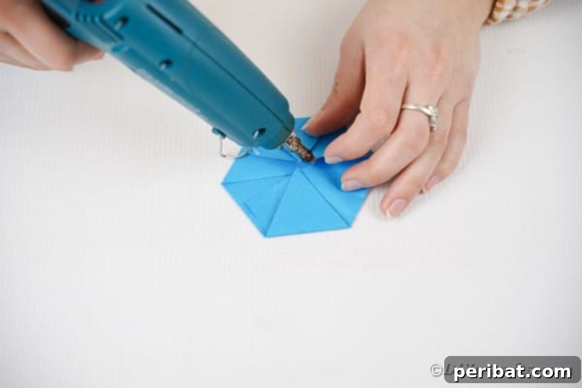 Vibrant DIY Paper Straw Desk Caddy 21 Hands are shown gluing the folds of a paper polygon together, securing its shape for the organizer's base.