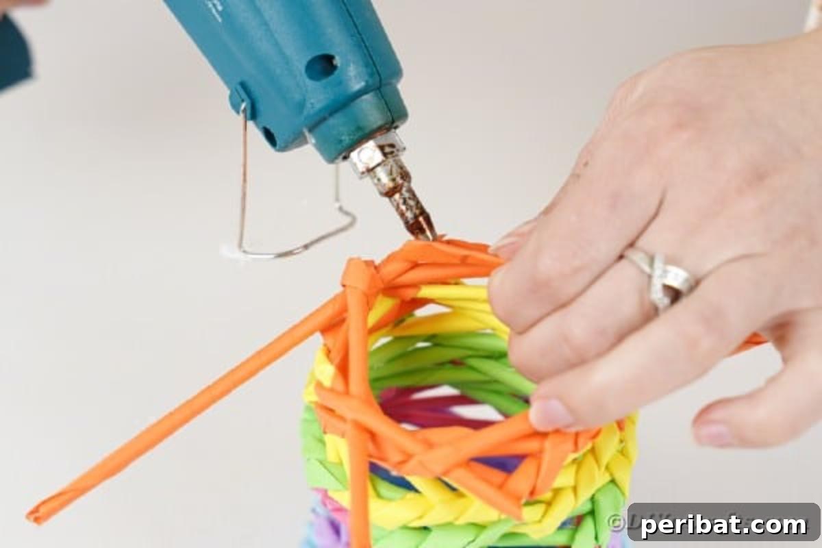 Vibrant DIY Paper Straw Desk Caddy 28 A hand is applying glue to secure the final paper straws at the top of the rainbow organizer.