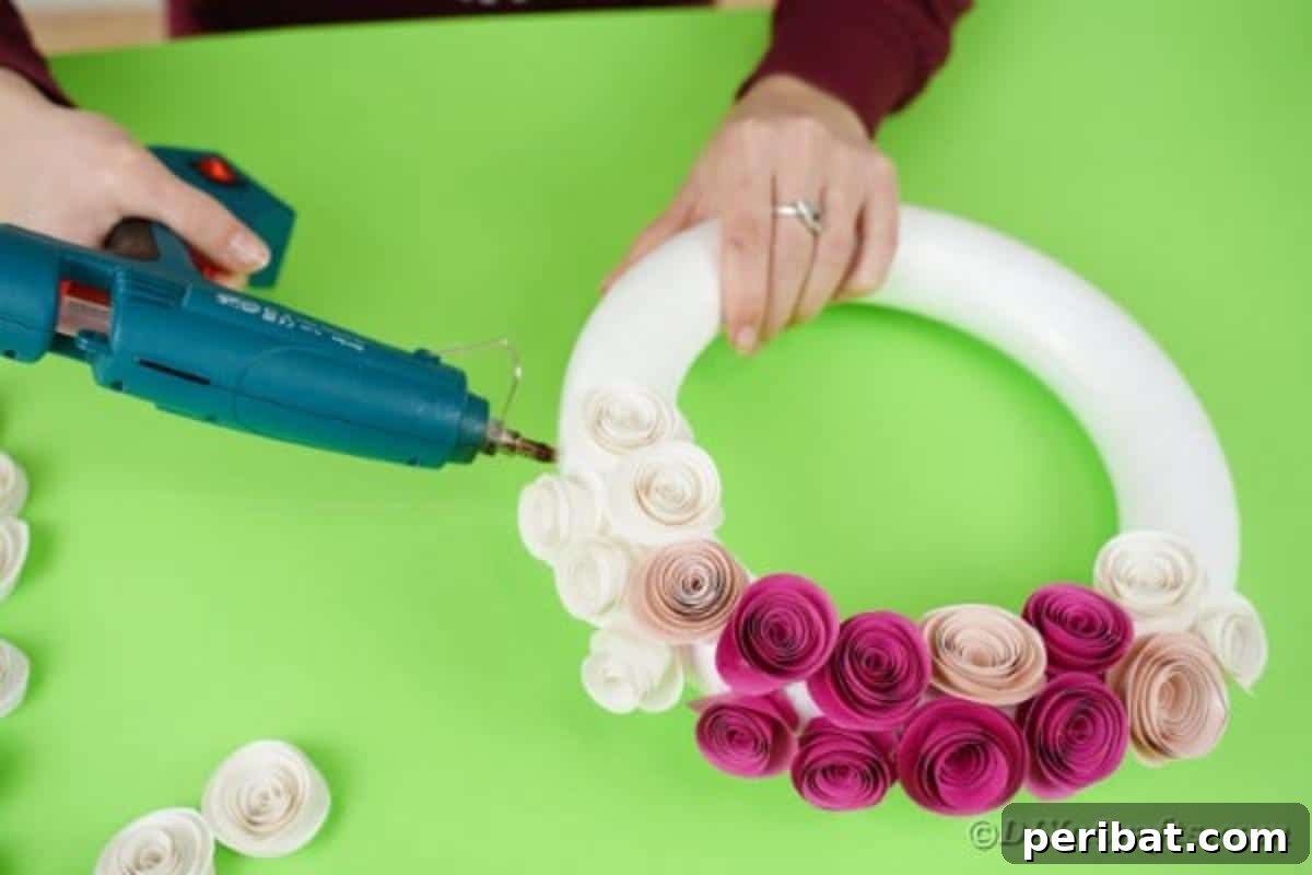 Enchanting Quilled Unicorn Wreath 11 Hands carefully gluing white rolled paper flowers onto a styrofoam wreath form, showing the process of covering the wreath base with the floral elements.