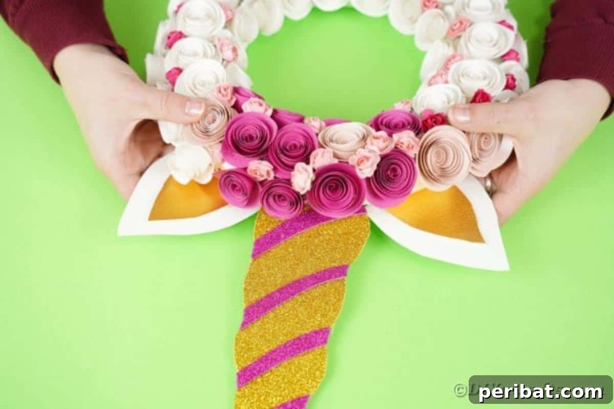 Enchanting Quilled Unicorn Wreath 18 The golden unicorn horn, decorated with pink glitter strips, securely glued onto the top-center of the floral wreath, completing the unicorn's face.