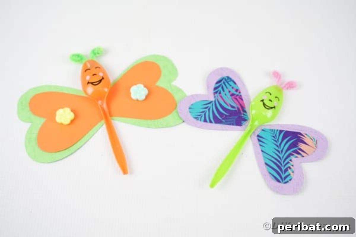 Two vibrant spoon butterflies, one green and one orange, adorned with mini flowers, resting on a clean white table, showcasing the final decorative touches.