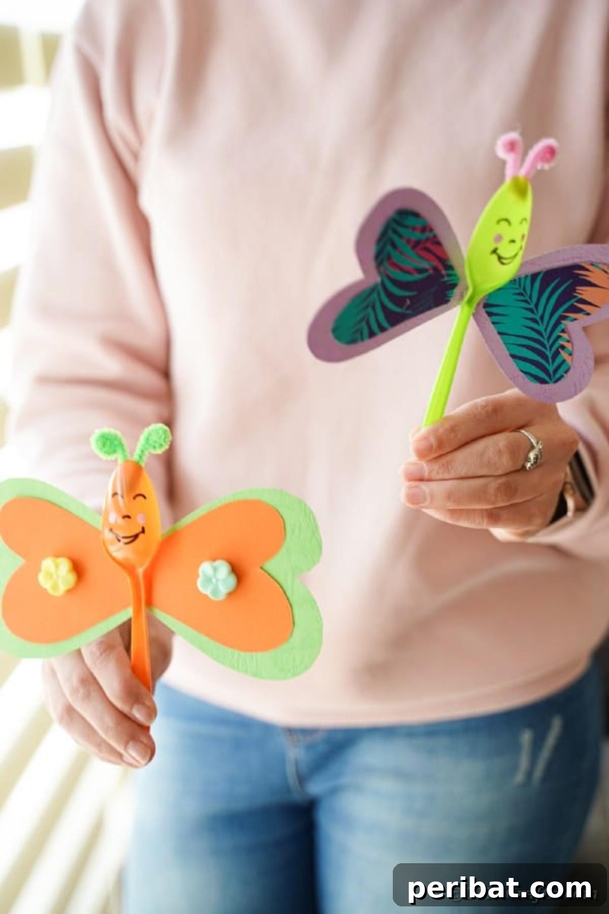 A woman's hands delicately holding a pair of colorful upcycled spoon butterflies, highlighting their size and handcrafted detail.
