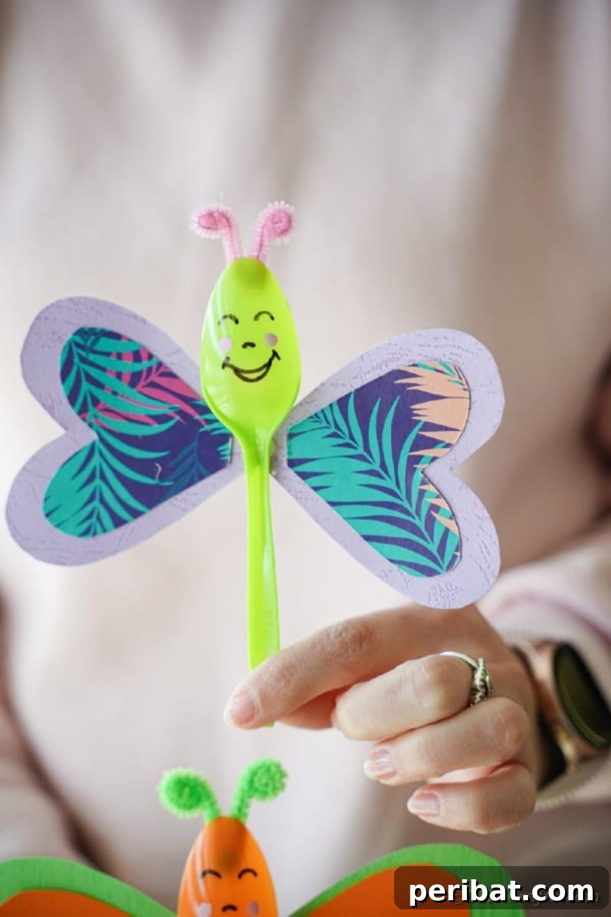 A striking blue and green upcycled spoon butterfly, showcasing its intricate paper wings and charming painted face against a bright backdrop.
