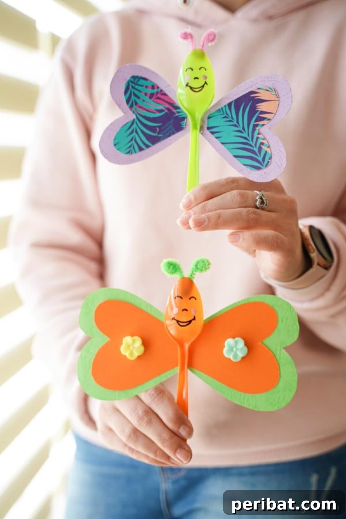 A woman's hands gently holding two colorful upcycled spoon butterflies, presenting the handmade crafts with pride and showcasing their beauty.