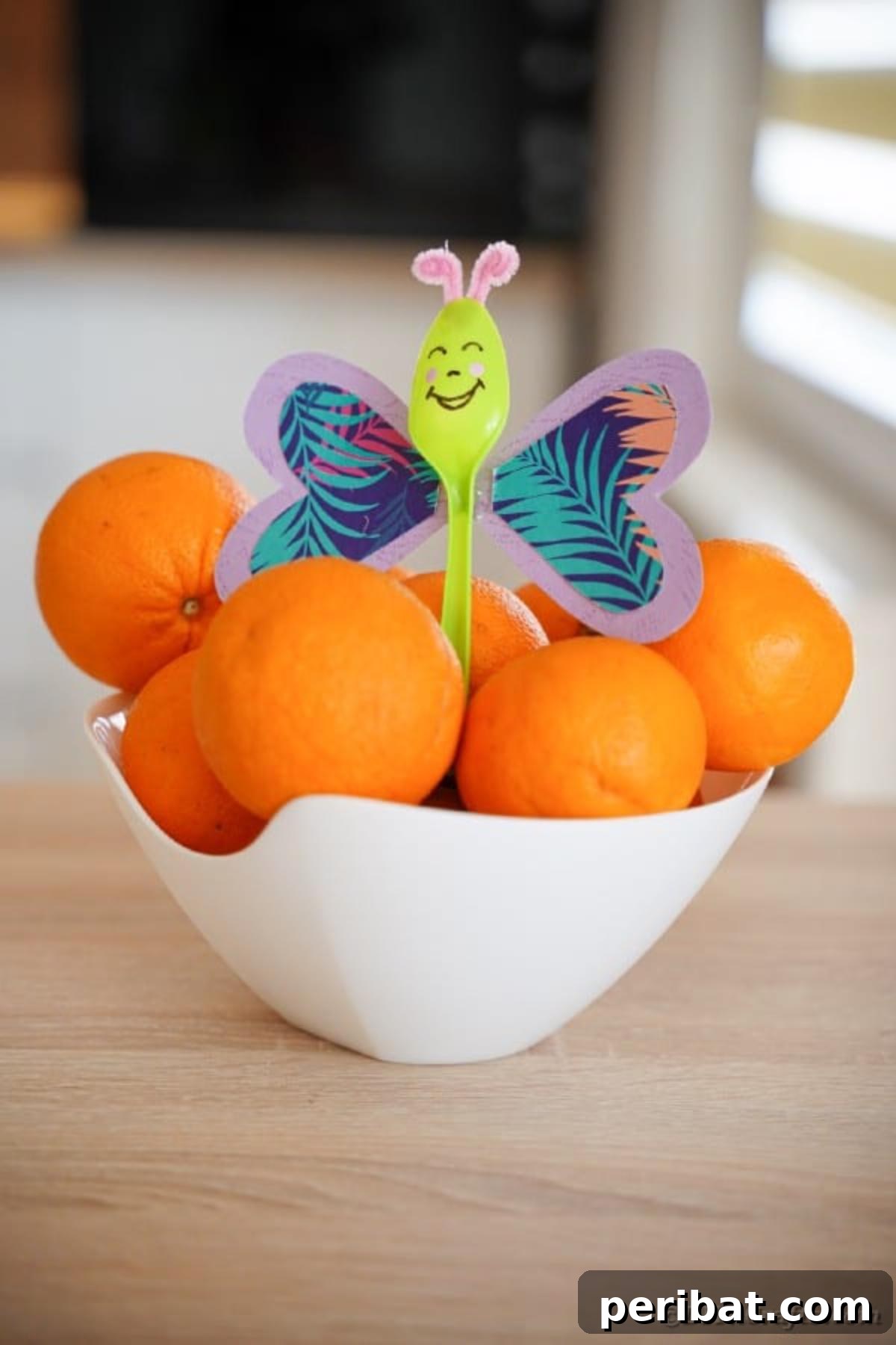 A beautiful purple upcycled spoon butterfly charmingly displayed among a cluster of bright, juicy oranges, adding a playful touch to kitchen decor.