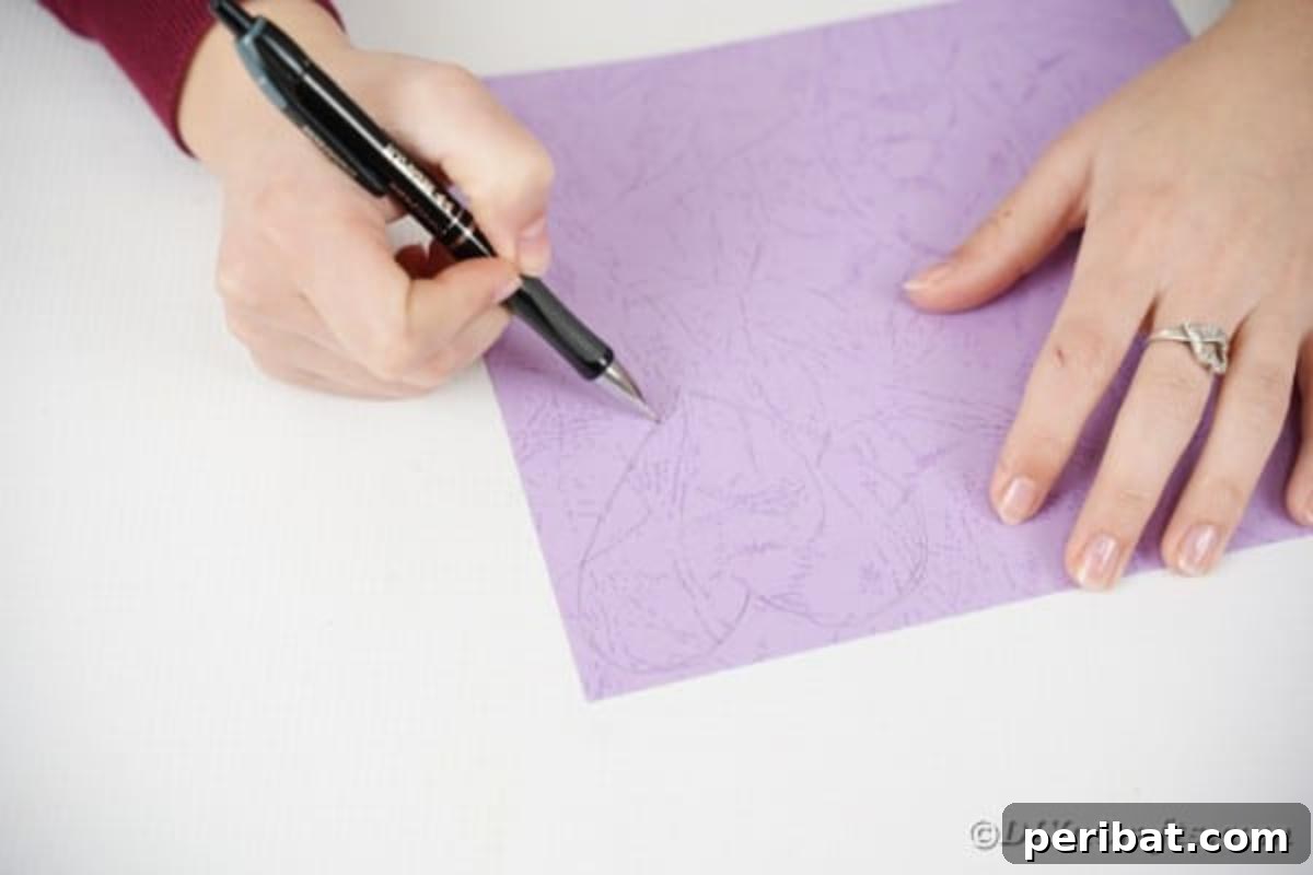 A hand drawing the outline of a butterfly wing onto a piece of solid colored craft paper, marking the first step in the creative process.