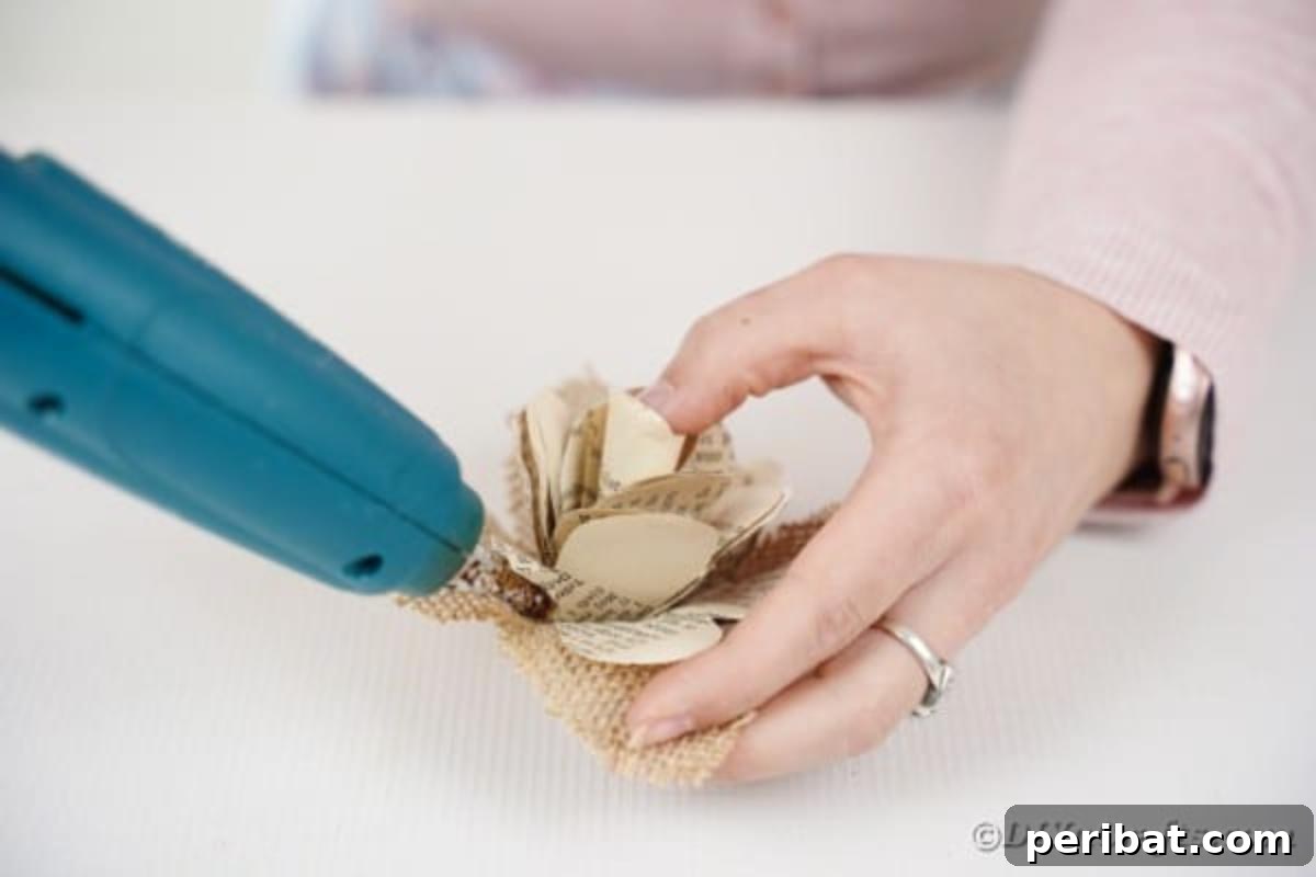 A hand fluffing a paper rose with burlap leaves to enhance its realistic look.