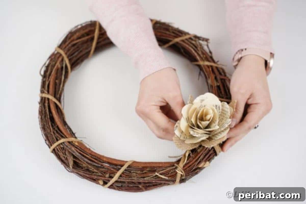 A finished paper rose being glued onto a grapevine wreath form, starting the assembly of the wreath.