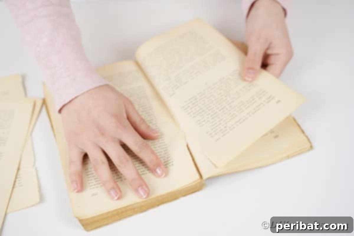 Hands carefully tearing a page out of an old book, starting the crafting process for the wreath.