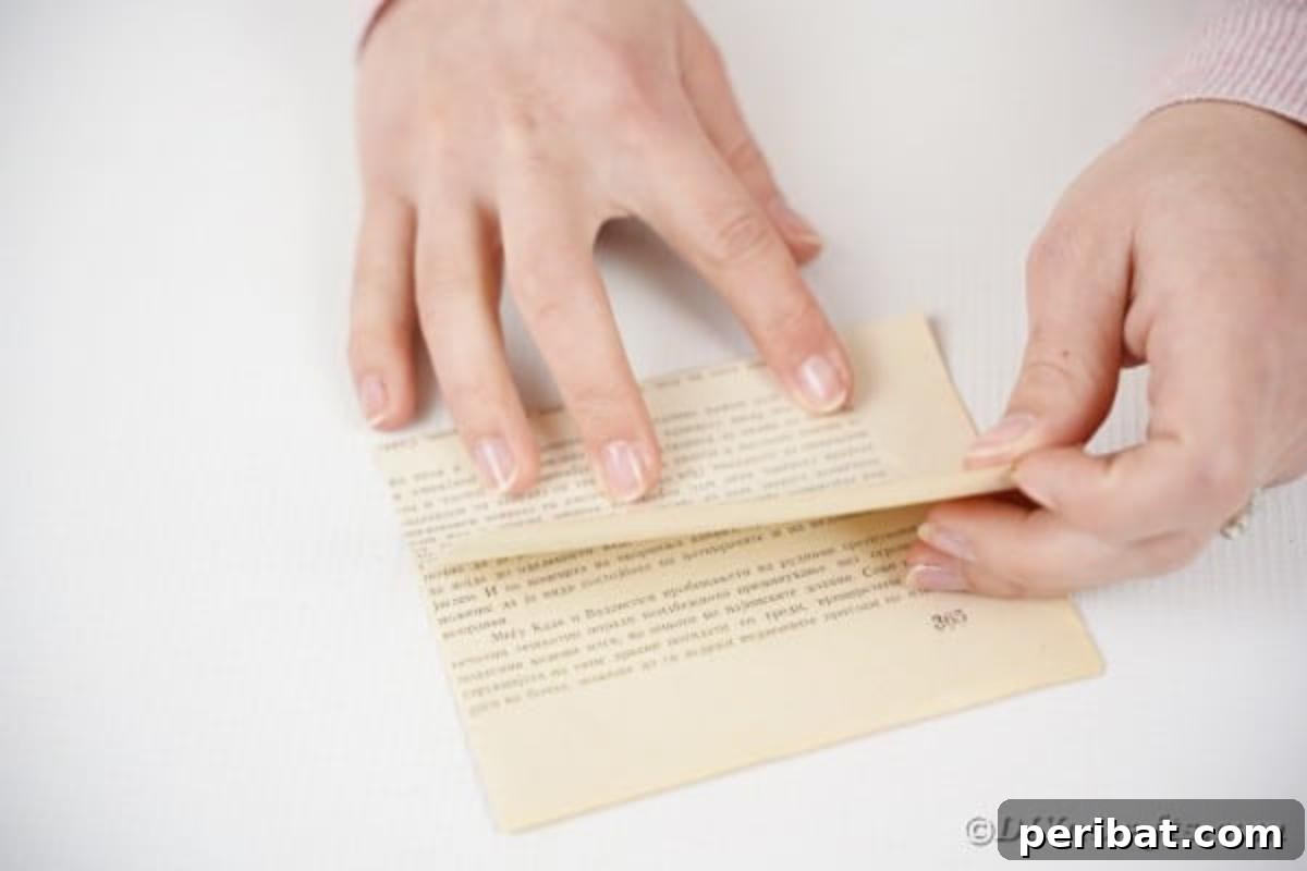 A book page being folded in half horizontally, a step in making paper roses.