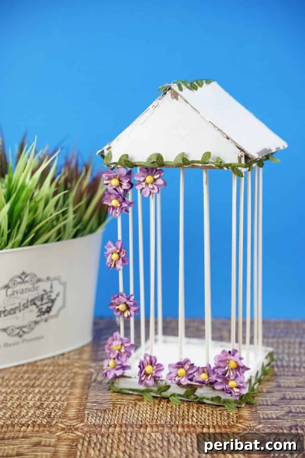 Crafting a Beautiful Floral Birdcage Display 25 Birdcage by Flower Pot with Blue Background - A decorative homemade birdcage, with white bars and vibrant purple flowers, positioned next to a terracotta flower pot against a soft blue wall, creating a serene and inviting display. Excellent for DIY enthusiasts.