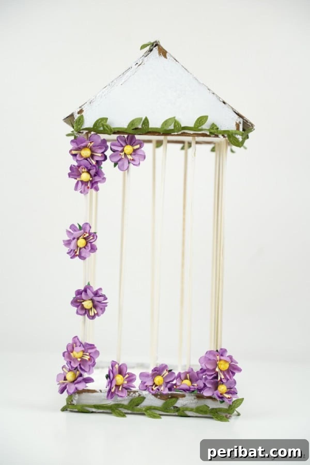 Crafting a Beautiful Floral Birdcage Display 26 White Birdcage with Purple Flowers on White Surface - A close-up shot of a decorative DIY birdcage with a distressed white finish, adorned with purple artificial flowers and green vines, resting on a clean white surface. Highlights the intricate details for craft lovers.