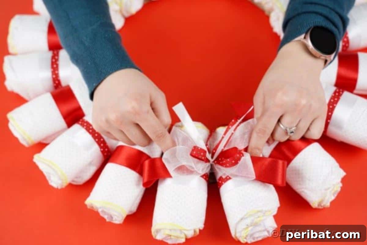 A decorative bow being added to the top center of the diaper wreath