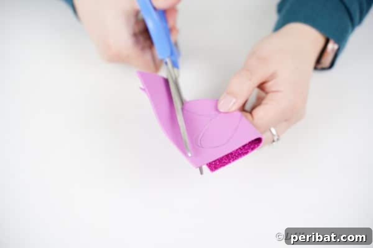 Create Vibrant Craft Stick Dragonflies for Kids 9 A child's hand cutting out a pair of connected dragonfly wings from glitter foam paper, folded in half for symmetry.