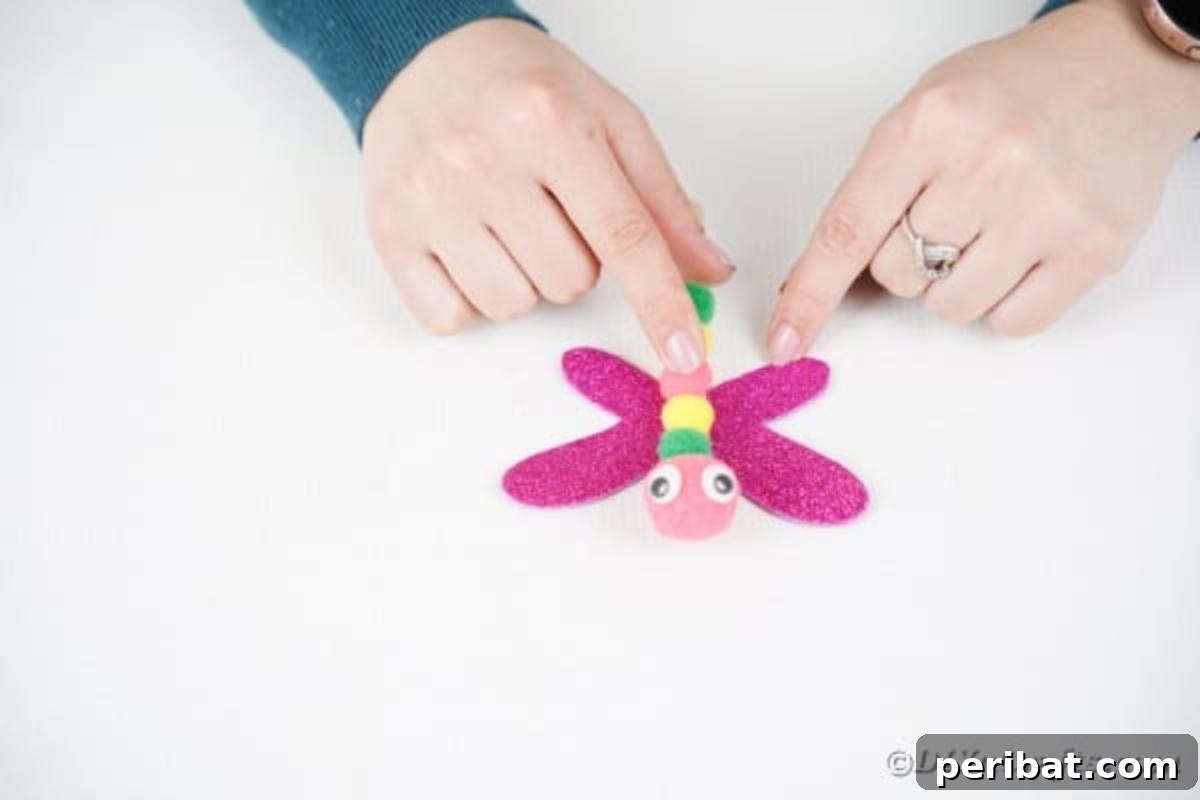 Create Vibrant Craft Stick Dragonflies for Kids 11 A craft stick dragonfly body being glued onto the center of its glitter foam wings, securing the two main parts of the craft.