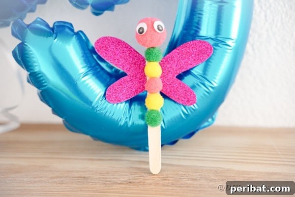 Vibrant craft stick dragonfly against a soft blue background, showcasing its finished design for a kids' craft project.
