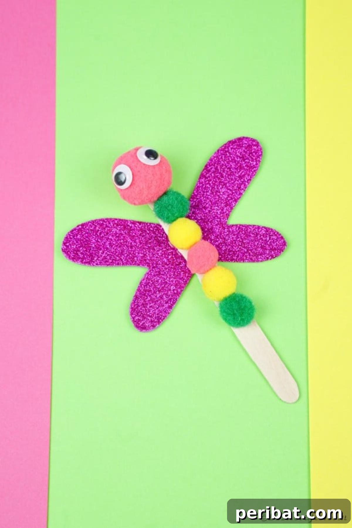 Create Vibrant Craft Stick Dragonflies for Kids 17 Several colorful craft stick dragonflies with pom-pom bodies and glitter wings arranged creatively on a vibrant green paper background.
