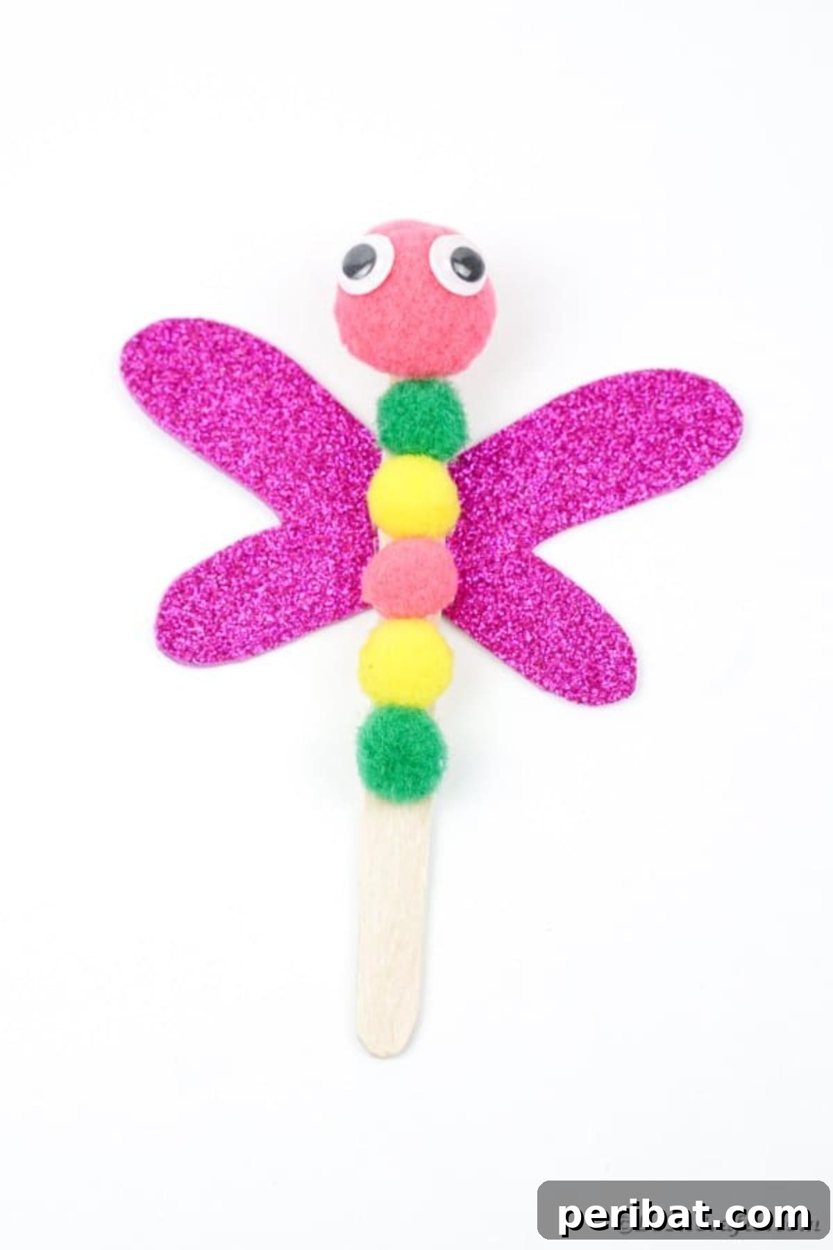 Create Vibrant Craft Stick Dragonflies for Kids 19 A completed craft stick dragonfly, featuring a multi-colored pom-pom body and glittery wings, displayed on a clean white surface.