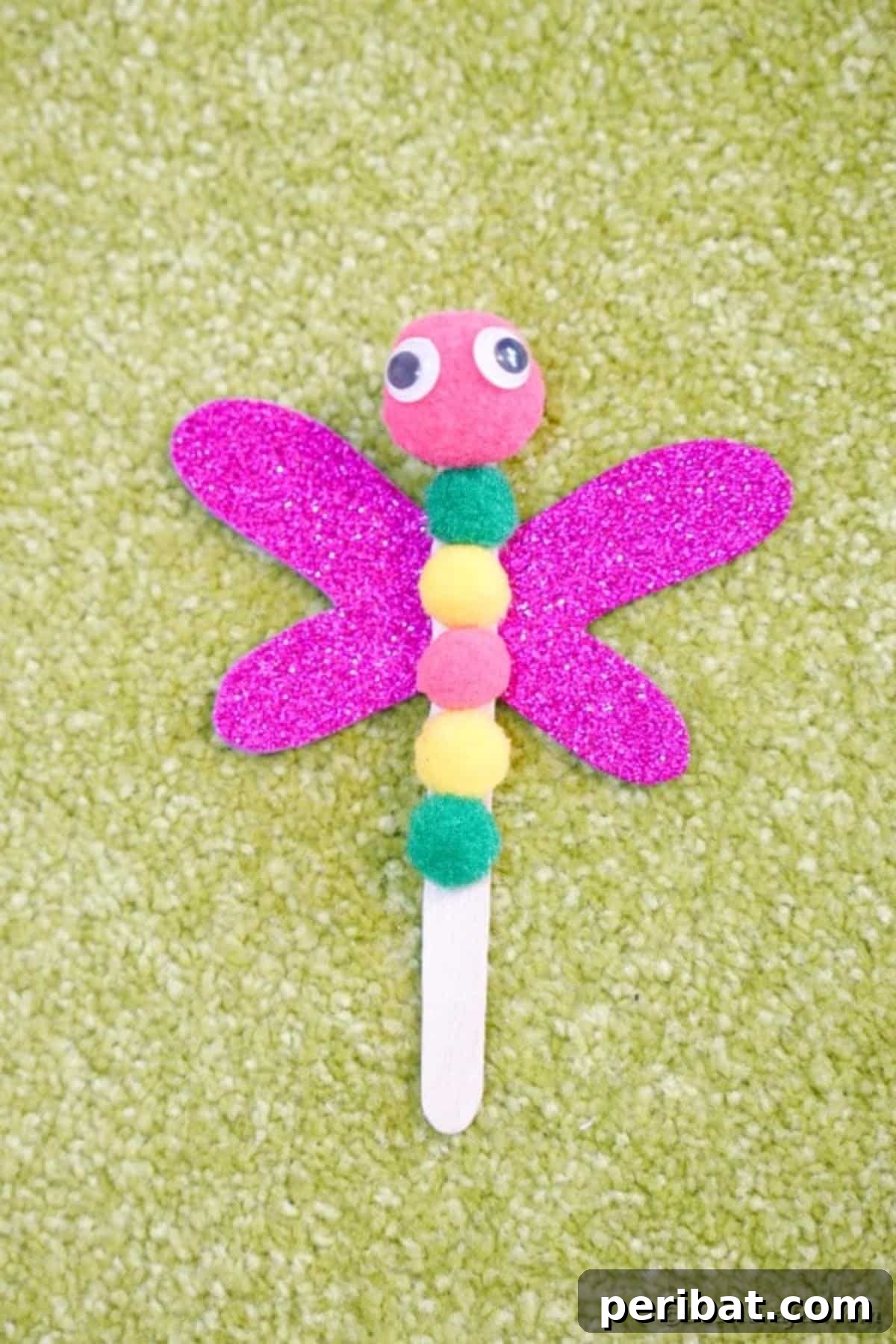 Create Vibrant Craft Stick Dragonflies for Kids 20 A simple, colorful craft stick dragonfly craft lying on a bed of fresh green grass, highlighting its natural setting.