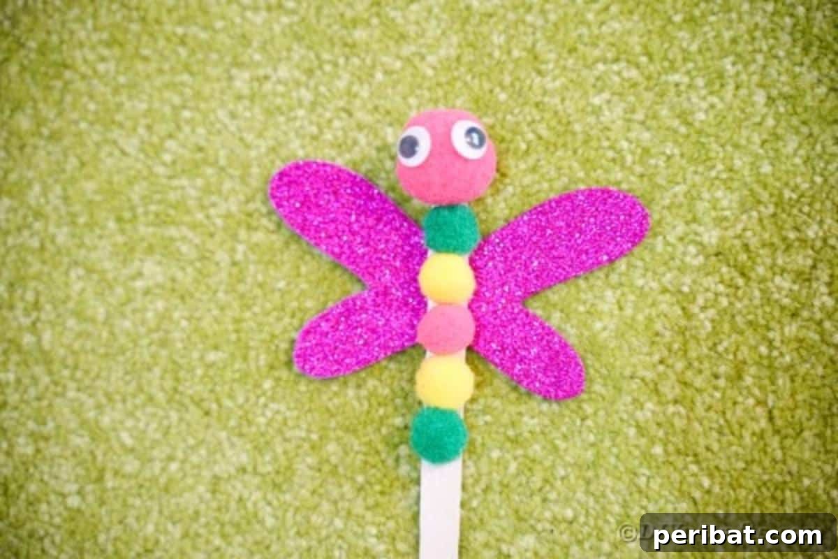 Create Vibrant Craft Stick Dragonflies for Kids 13 A simple yet charming craft stick dragonfly resting on a bed of green grass, highlighting its textured body and shiny wings.