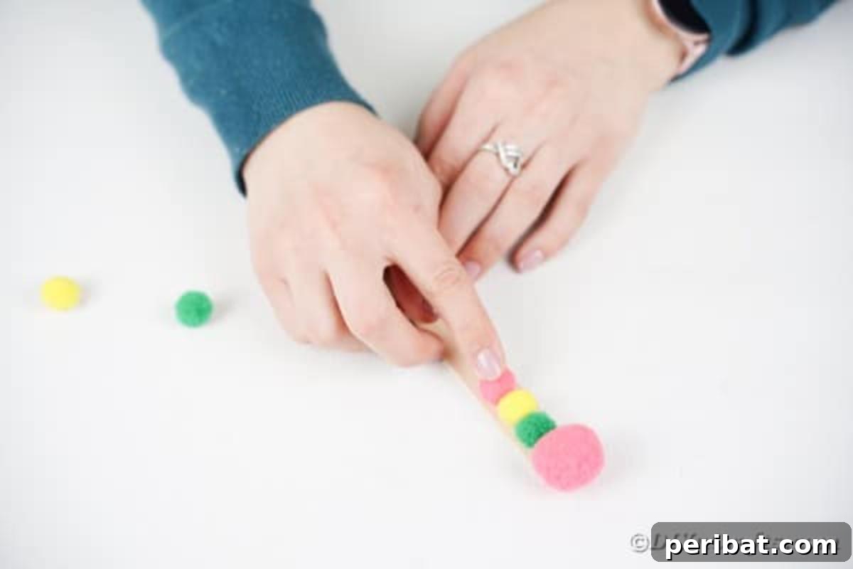 Create Vibrant Craft Stick Dragonflies for Kids 7 Attaching several small, colorful pom-poms in a row along a craft stick to form the body of the DIY dragonfly.