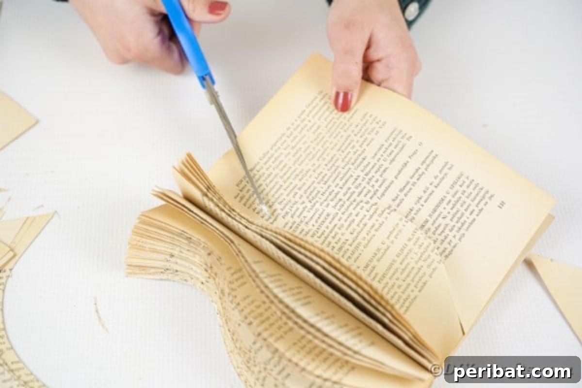 A person using scissors to meticulously cut out the last few pages of a book, refining the vase shape after initial cuts with a craft knife.