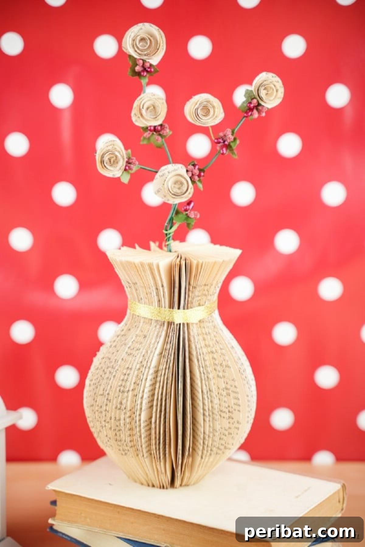 A beautifully textured paper vase made from old book pages, presented against a vibrant red polka dot background, showcasing its unique form and decorative versatility.